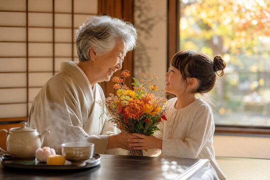 Granddaughter Giving Flowers to Grandmother for Respect for the Aged Day,敬老の日に孫から花束を受け取る祖母の温かな家族写真