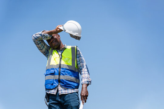 Tired Construction Worker Wiping Sweat Under the Hot Sun, Exhausted Engineer Taking a Break at Construction Site in Heat, Manual Labor in Extreme Weather, Worker Man Struggling with Heat Stress