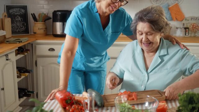 Smiling senior woman prepares a healthy salad with her caregiver, chopping fresh vegetables while sharing joyful moments in a cozy home kitchen.