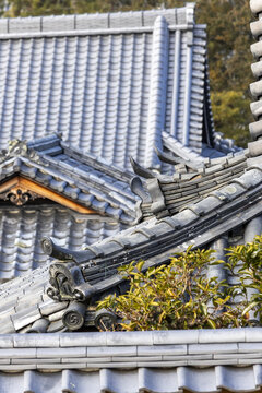 View of traditional Japanese temple rooftops with grey ceramic tiles and ornate ridge ornaments in Nara, Nara, Japan.