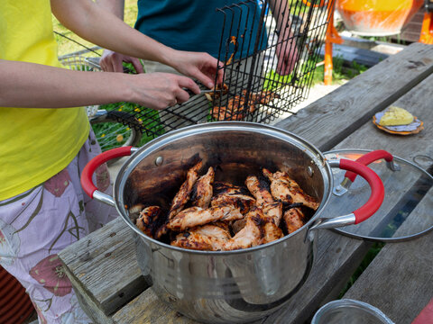 A man and a woman are cooking chicken or meat on a grill. There is a large pan with fried meat on the wooden table. Picnic in nature.