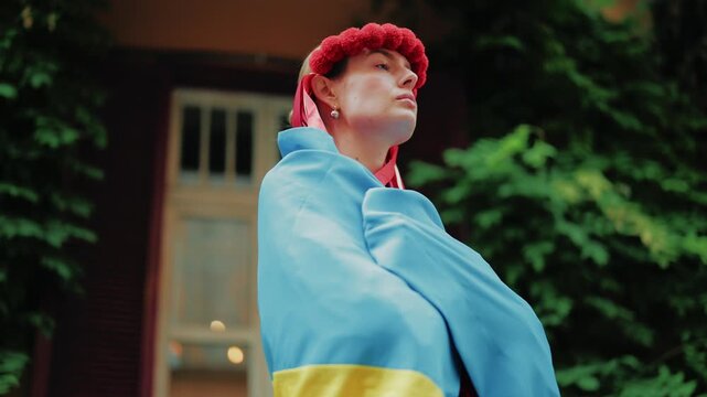 Woman in a traditional vyshyvanka and red floral wreath poses while holding a blue and yellow Ukrainian flag. The shot captures a dynamic movement, emphasizing national spirit and cultural pride in an
