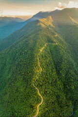 Breathtaking aerial view of a winding road running along the ridge of lush green mountains illuminated by golden sunrise light. © Nguyen Phong