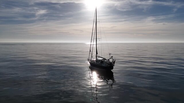 Circular drone move around sailboat on shimmering calm sea.