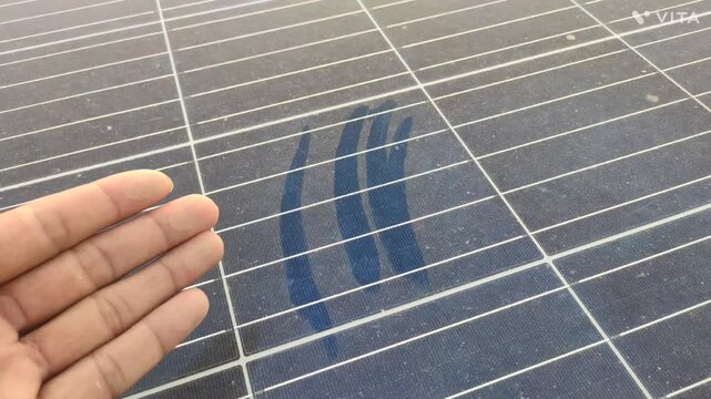 A solar panel surface covered with dust, featuring a prominent handprint wiping some of the dust away