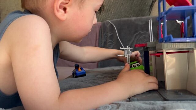 A young boy focuses on playing with colorful toy cars and a multi-level garage playset on a grey surface. Boy Playing with Toy Cars and Garage Playset