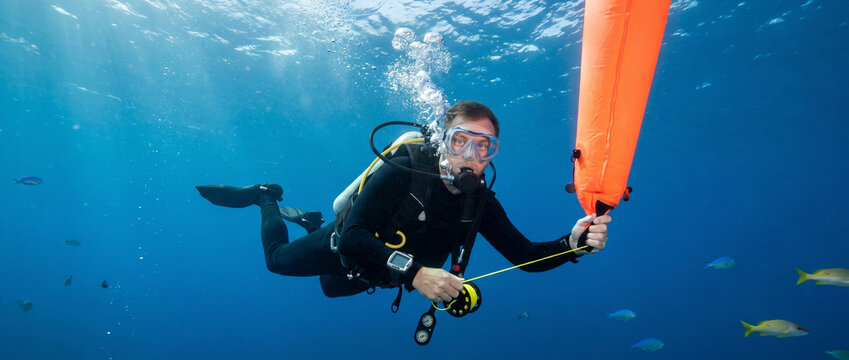 Diver holding a surface marker buoy underwater in clear blue ocean  