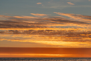 Fototapeta premium Sunset over water, vibrant hues orange, pink, yellow, scattered clouds, sky reflection on water, horizon line, vastness, tranquility, no objects or people, distant perspective, warm lighting, reali