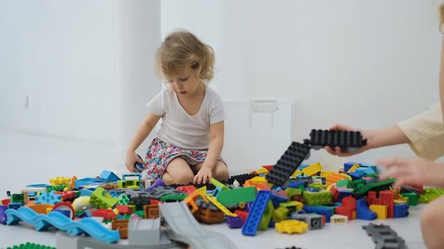 Young child sitting among a large scattered pile of colorful building blocks picking and sorting pieces on the floor. Childhood and play concept