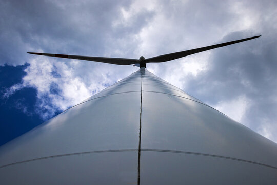 View of a tall white wind turbine tower reaching towards the blades against a dramatic cloudy sky Germany.