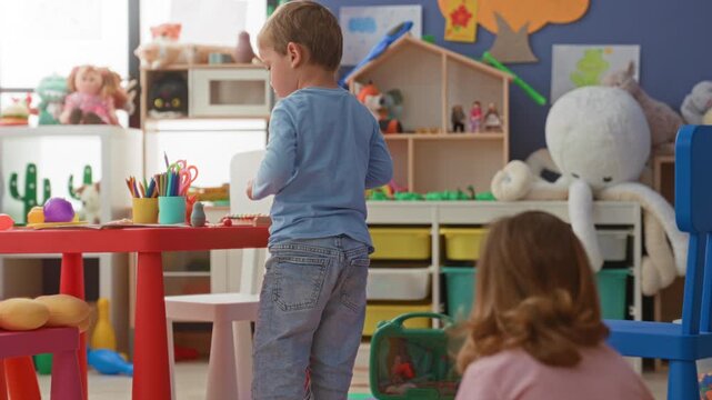 Girl and boy playing with toys, girl reaches for a pink chair while boy sorts crayons at a small table in a building playroom; playfulness curiosity.