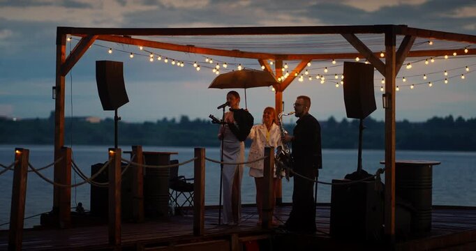 Duet on a Lakeside Stage at Dusk Under String Lights