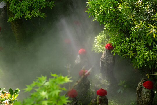Stone Jizo statues with red hats surrounded by mist and green foliage, Japan