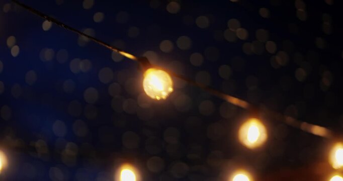 Single warm bulb on a diagonal wire with bokeh night lights