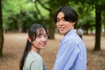 Fototapeta premium 新緑の木々を背景に微笑む若いカップルのポートレート