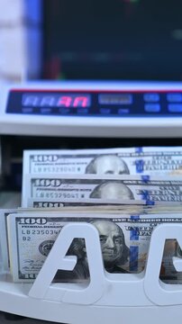 A close up view of an automatic money counter machine quickly counting one hundred dollar bills, displaying a digital count.