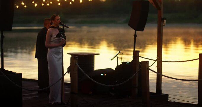 Female saxophonist performing on a lakeside dock at sunset