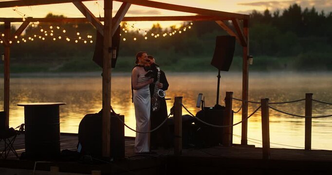 Female Singer and Saxophonist Duet on Lakeside Dock at Sunset