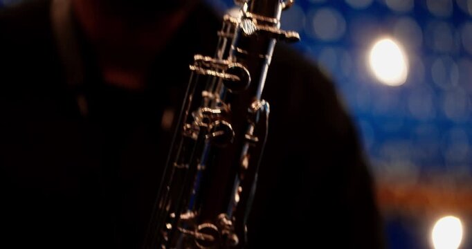 Close-up of tenor saxophone bell with musician in low-key blue stage lighting