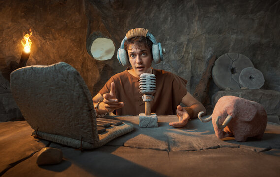 Funny Young Prehistoric Caveman Speaking into Stone Microphone for Podcast in a Cave