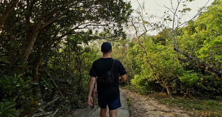 Obraz premium Back view of man walking on forest trail. Dense green foliage. Outdoor adventure. Active lifestyle. Summer hiking.