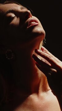 Stunning vertical close up of an attractive woman sensually stroking a cold ice cube on her neck and chest in slow motion