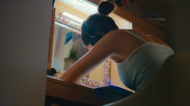 Rear view of a young female student sitting at her desk, wearing over-ear headphones and listening to music while trying to focus on textbook notes. Retro analog cinematic film look, 4k.