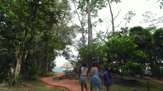 Mother and daughters walk along a red paved path under giant jungle trees toward the iconic viewing gazebo at Mission Lodge (Venn's Town) in Morne Seychellois National Park.30fps