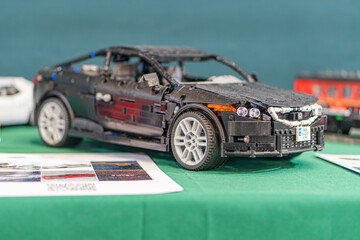 Naklejka premium Black and silver Lego replica of an Aston Martin DB9 toy car, elevated on a clear plastic stand against a green tablecloth Stacked white papers nearby - Kyiv, Ukraine - June 7, 2025