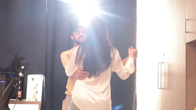 Young couple dancing together in sunlit room with bright morning light streaming through curtains