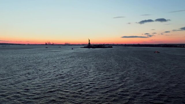 A breathtaking wide aerial drone shot approaching the iconic Statue of Liberty in New York Harbor. The camera glides smoothly across the water, revealing the world-famous monument standing proudly aga