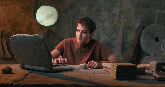 Funny Caveman Working on Stone Laptop and Hitting it with Hammer in Prehistoric Cave