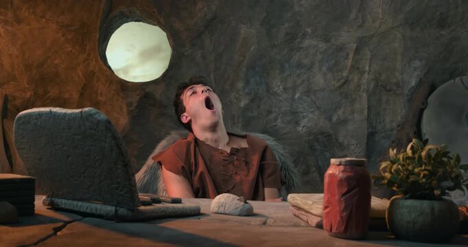 Funny Caveman Yawning and Feeling Tired in Front of Stone Laptop in Prehistoric Cave