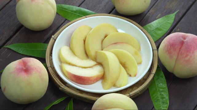 White Peaches with leaves and Slice of  Peach on white dish, Fresh White Peach on wooden basket in wooden Background.