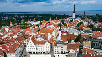 Obraz premium Tallinn, Estonia, showcasing the historic old town's rooftops, charming medieval architecture, and prominent church spires under a cloudy sky with the Baltic Sea in the distance