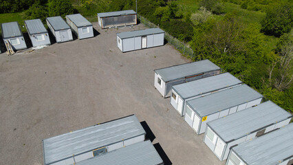 Portable cabins and construction containers are waiting on a gravel lot surrounded by green trees and foliage, providing temporary housing or office space © Dark Artistic