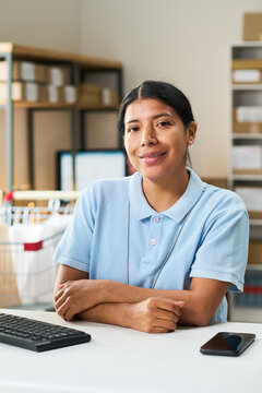 Portrait of young Latina woman working at order pickup desk, managing food delivery logistics and customer service. Useful for retail operations, courier app marketing, vertical