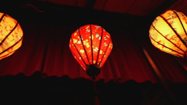 Close-Up motion along row of Glowing Vietnamese Silk Lanterns with Floral Pattern in dark interior