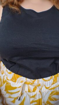 Close-up of a plus-size woman's hands tying the drawstring on her yellow patterned pants. Vertical video for body-positive casual summer fashion retail, morning routine, and apparel marketing ads.