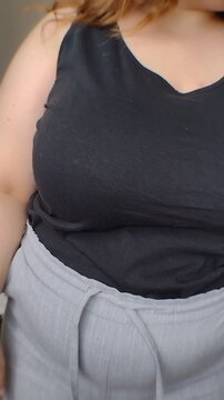 Close-up of a plus-size woman's hands tying the drawstring on her grey trousers. Vertical video for body-positive casual fashion retail, daily morning routine, and apparel marketing ads.