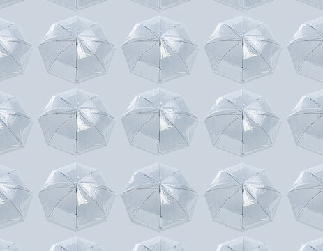 Seamless repeating pattern of multiple clear umbrellas covered in glistening water droplets from recent rain, all viewed directly from an overhead perspective against a soft light blue gray background