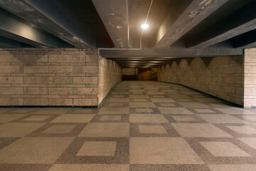 Fototapeta premium Illuminated underground pedestrian tunnel with patterned floor and stone walls