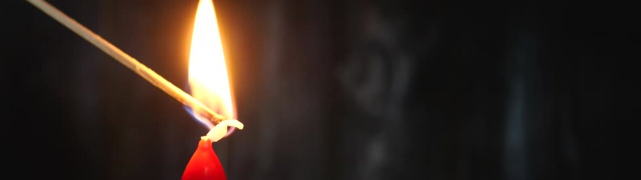 Matchstick bringing flame to a candle wick creating light and hope in a dim environment.