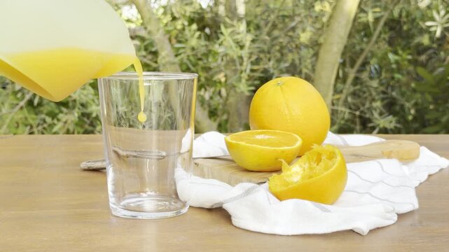 Fresh orange juice pouring into glass on outdoor table