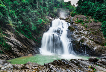 Obraz premium Beautiful waterfall at the mountain with blue sky and white cumulus clouds. Waterfall in tropical green tree forest. Waterfall is flowing in jungle. Nature abstract background. Granite rock mountain.