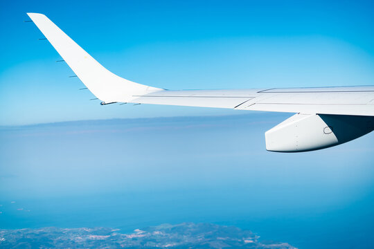 Airplane wing above clouds with scenic view of city and landscape below during an international commercial airline flight. Aviation travel, air transportation and global connectivity under a blue sky.