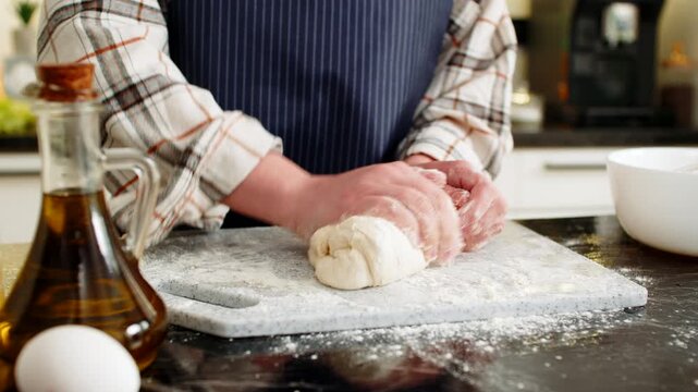 Woman prepares baking dough by hand kneading soft mass on floured board with eggs milk and oil nearby. Simple recipe process home cooking for bread pizza or buns closeup with apron in home spaces.