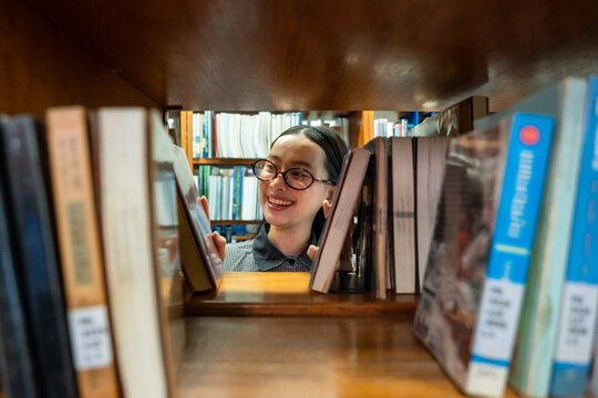 Asian young girl reader searching for books to read in quiet library. 