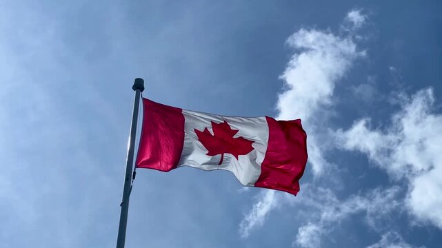 Canadian maple leaf flag billowing in the wind under blue sky