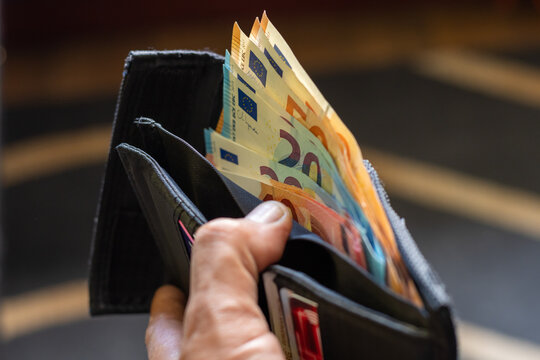 Close up of a man hand holding an open black wallet filled with Euro banknotes with copy space.
